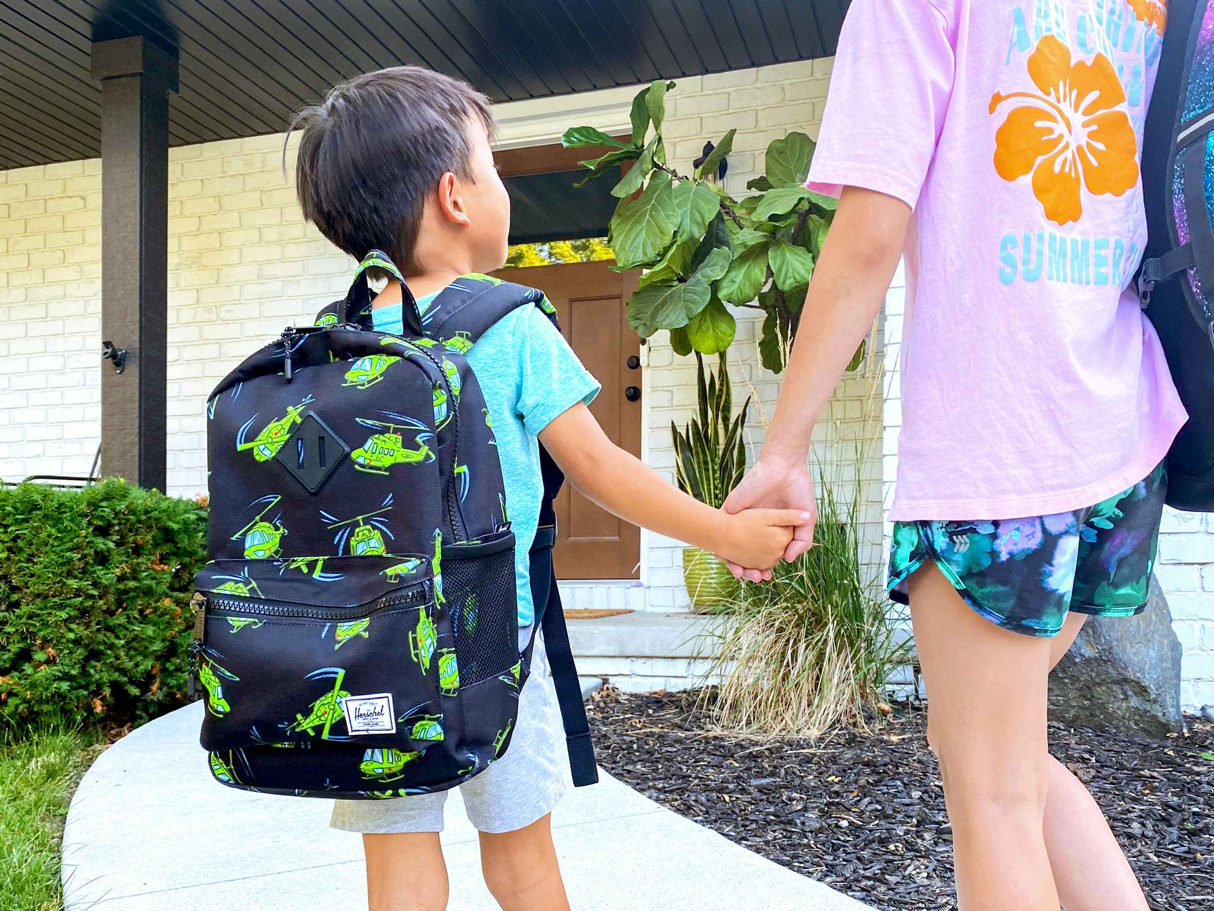 two kids wearing backpacks walking up to a house