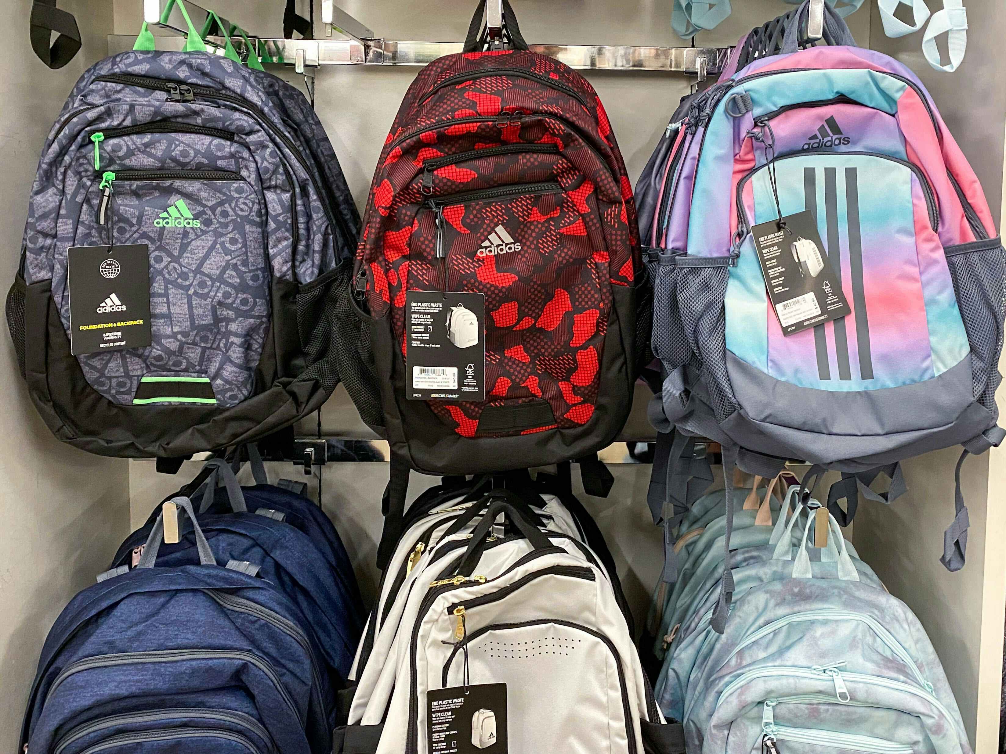 Some adidas backpacks hanging on display inside a store.