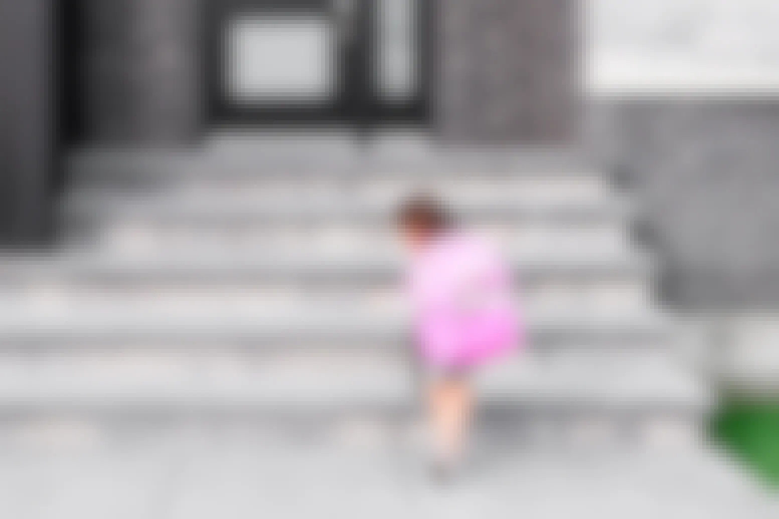 A little girl wearing a pink L.L.Bean backpack, walking toward the steps of a school.
