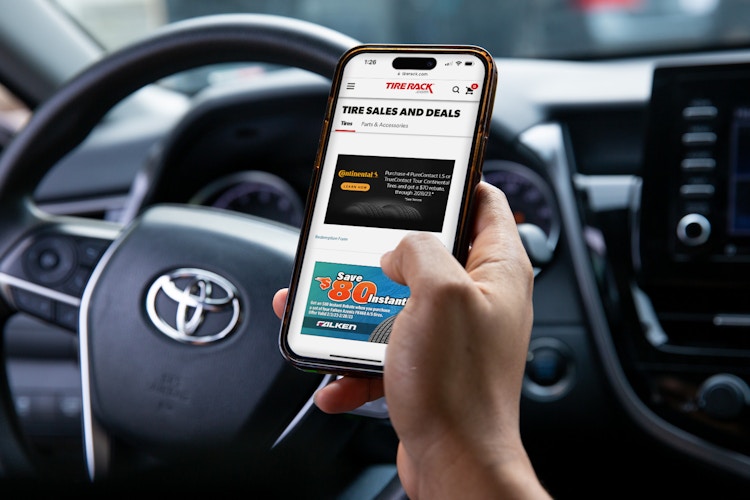 A person sitting in their parked car, looking up tire deals on TireRack.com
