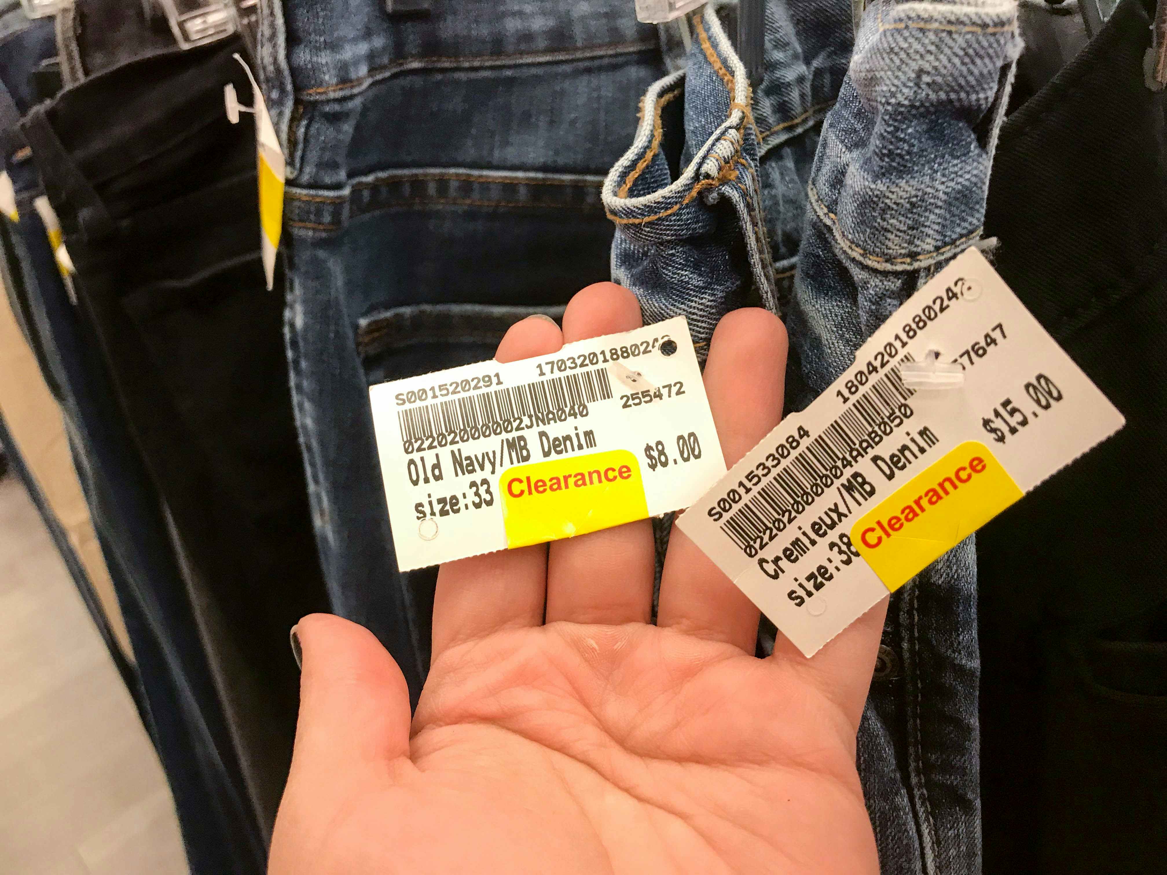 Someone holding up two clearance tags on some jeans on a rack at Plato's Closet