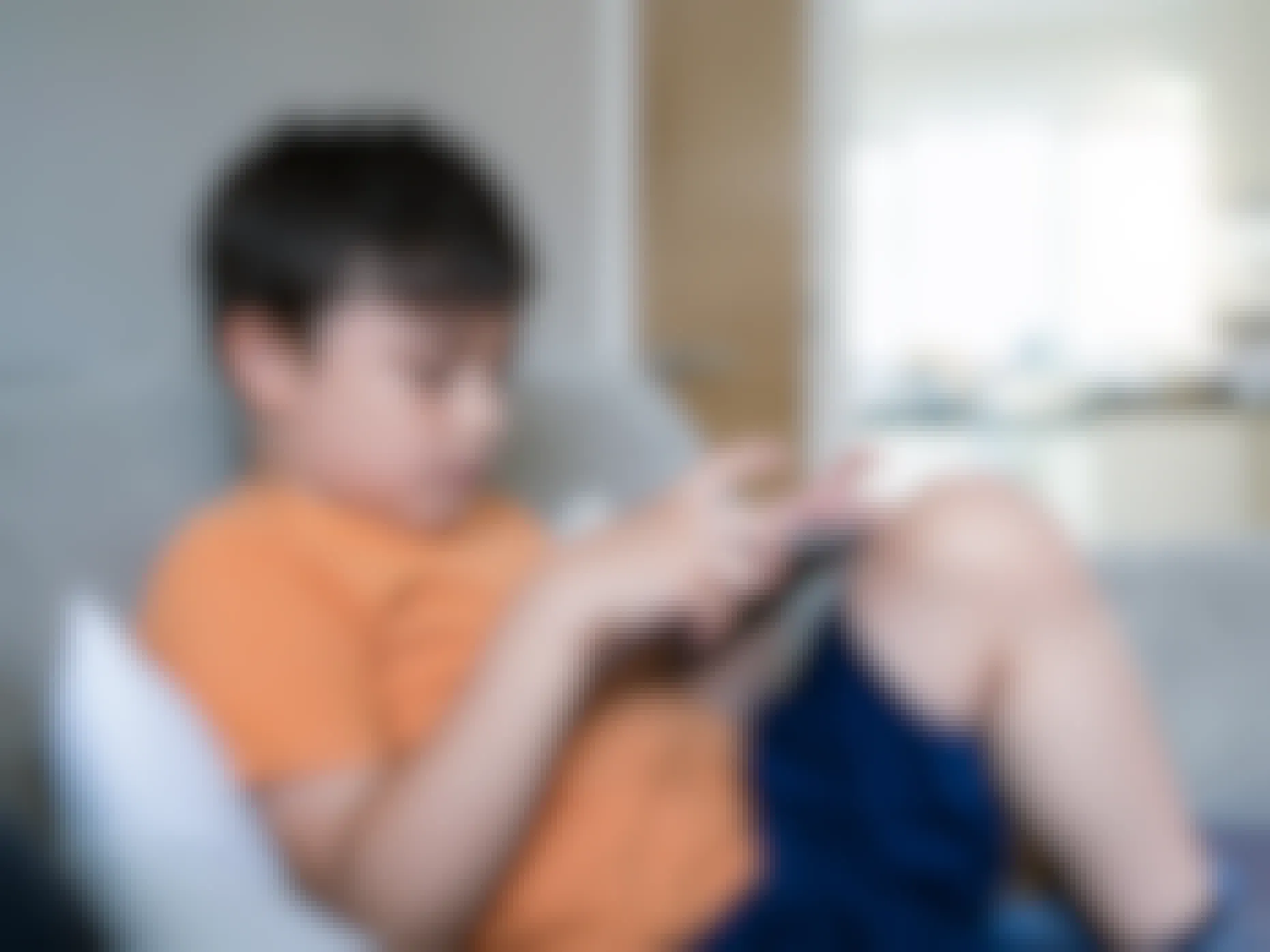 A child sitting on a couch, holding and looking down at an e-reading device.