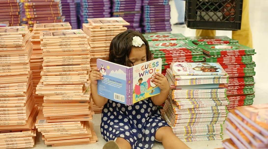 FirstBook.org girl reading books with a big pile behind her