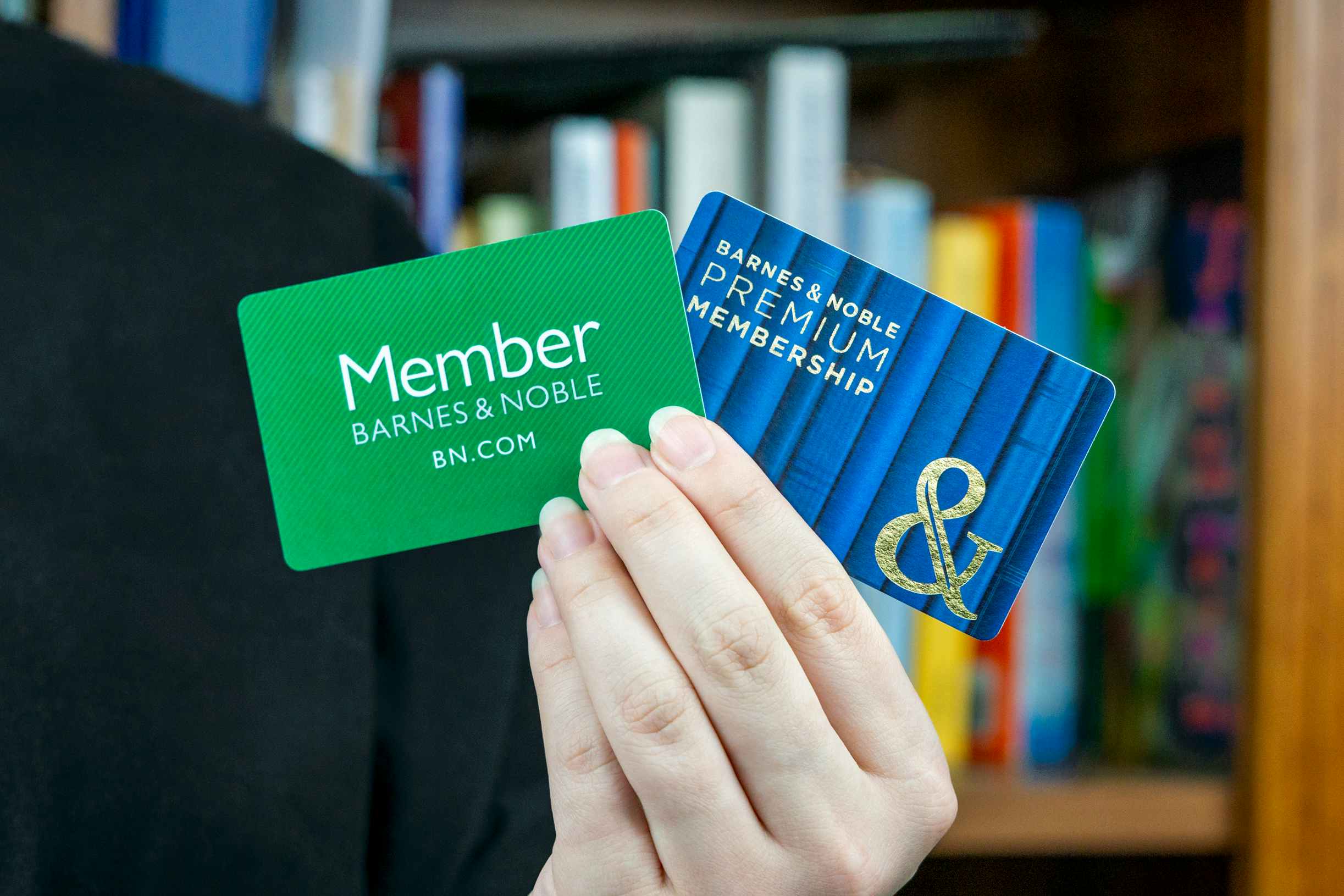 someone standing near a bookshelf, holding up a free and premium barnes and noble membership card