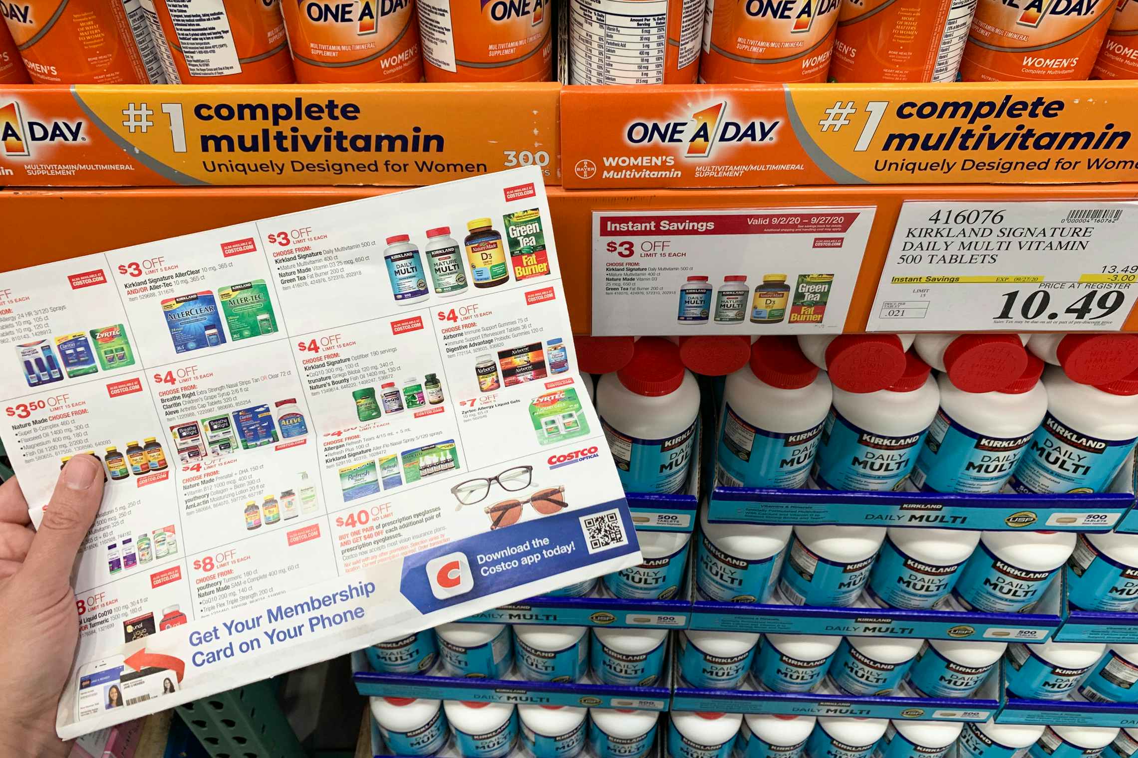 Costco coupon book with Kirkland vitamins on the page and the shelf behind it