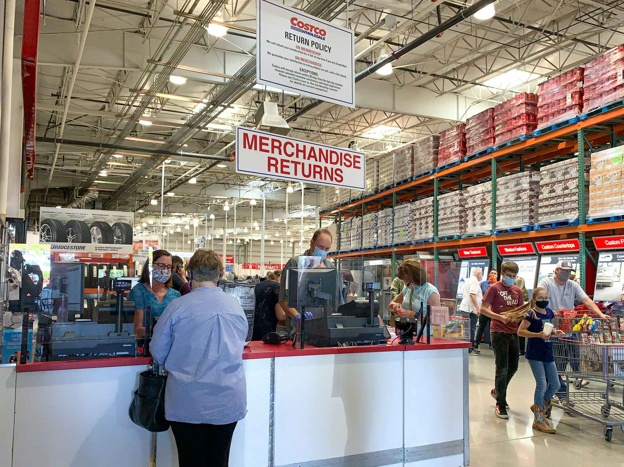 A person standing at a counter at Costco with a sign that reads "Merchandise Returns" hanging above their head.