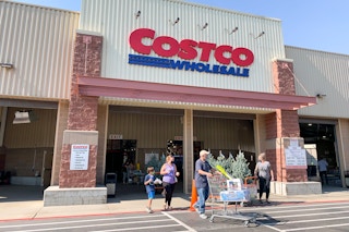 Costco store front with people exiting with a cart full of purchased goods.