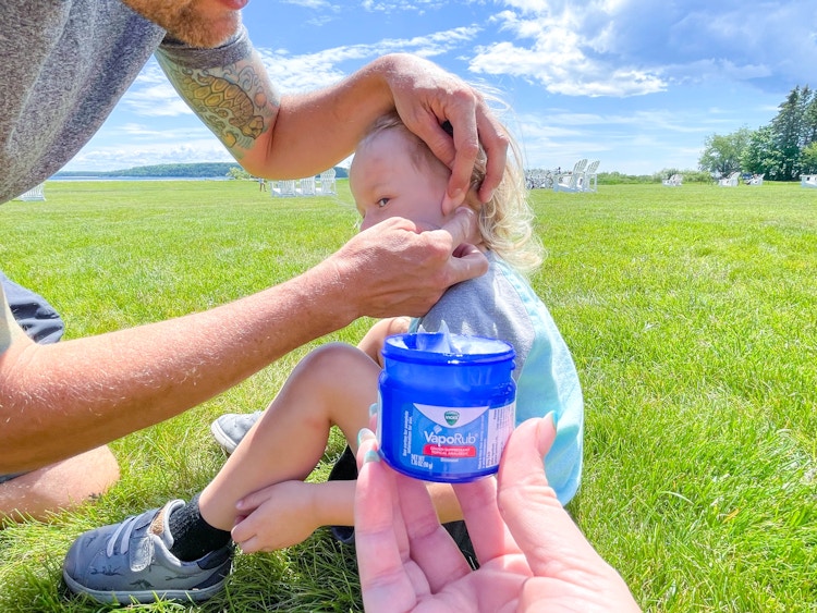 little boy by flowers having vicks vaporub behind ear