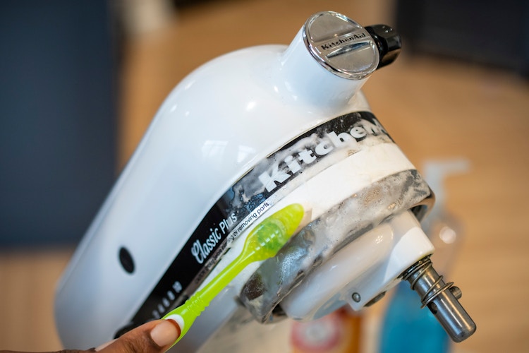 A person using a toothbrush to clean a KitchenAid mixer with a baking soda paste