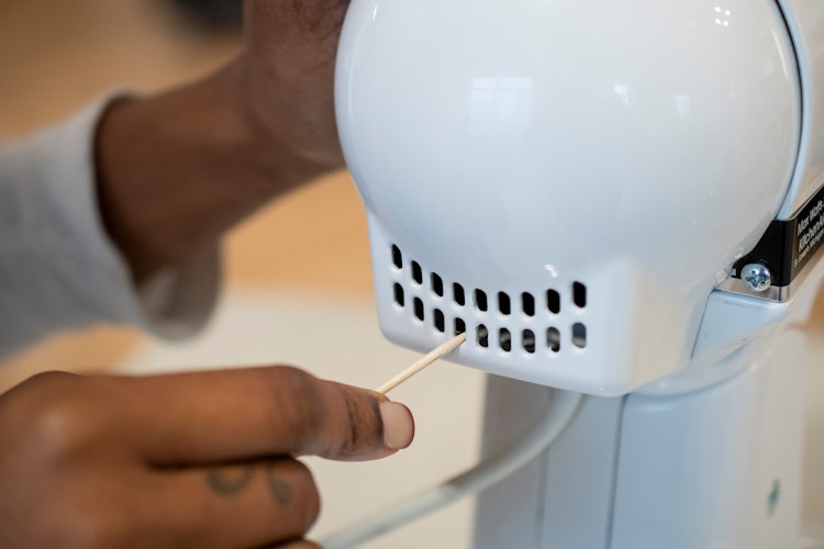 A person using a toothpick to clean out the vent on a KitchenAid mixer