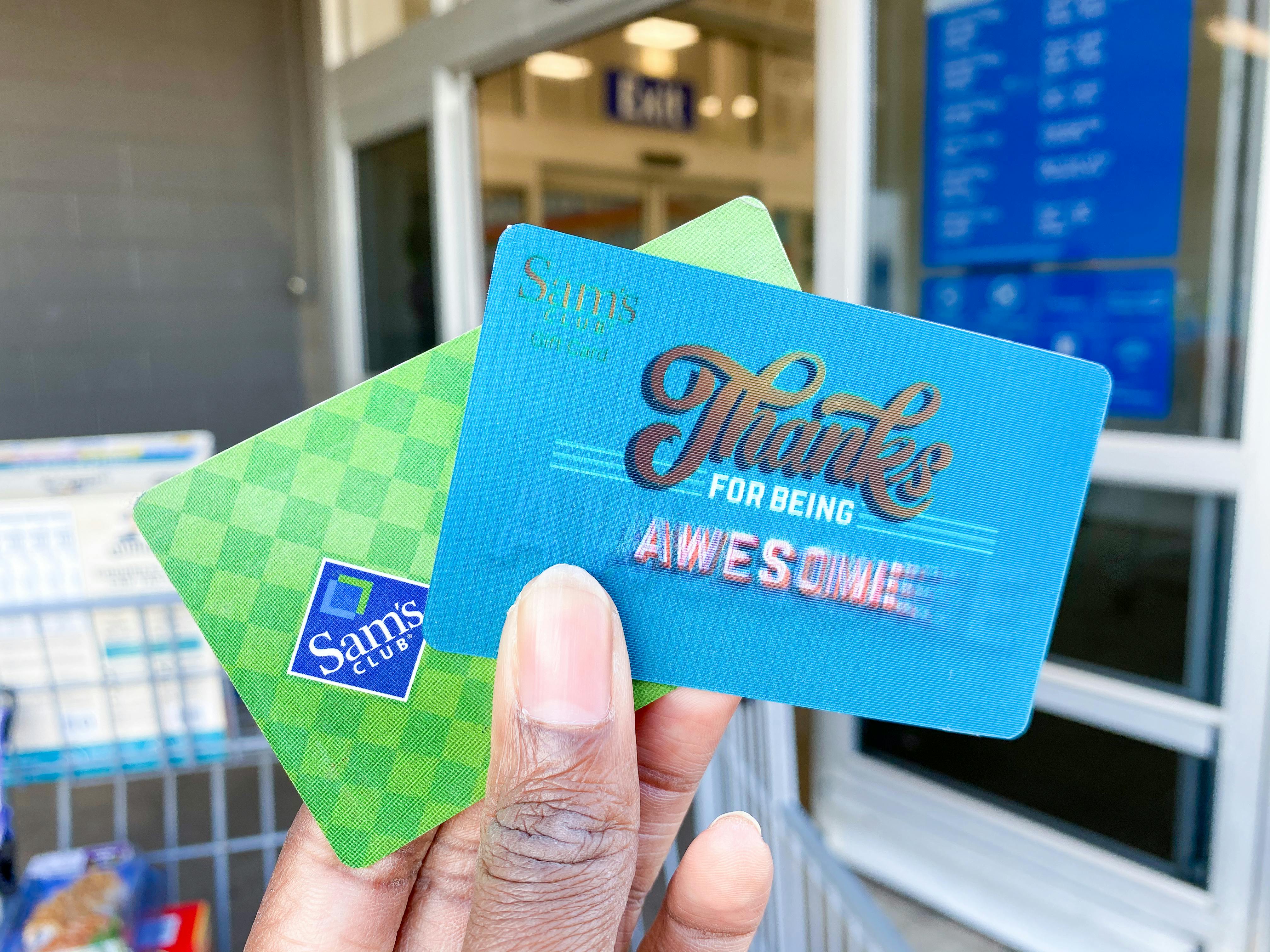 Sam's Club membership card and Sams club gift card being held in hand in front of Sams club entrance