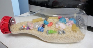 An clear plastic bottle with sand and toys in it.