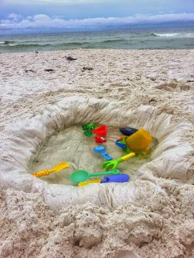 A pool made into the sand with a shower curtain liner at a beach.