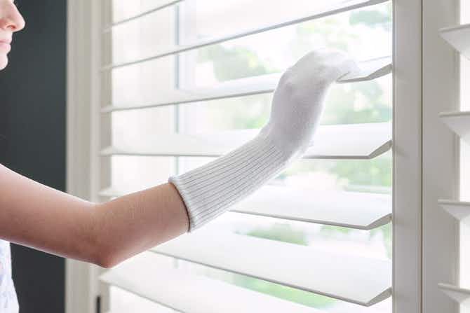 Someone using an old sock to clean and dust blinds.