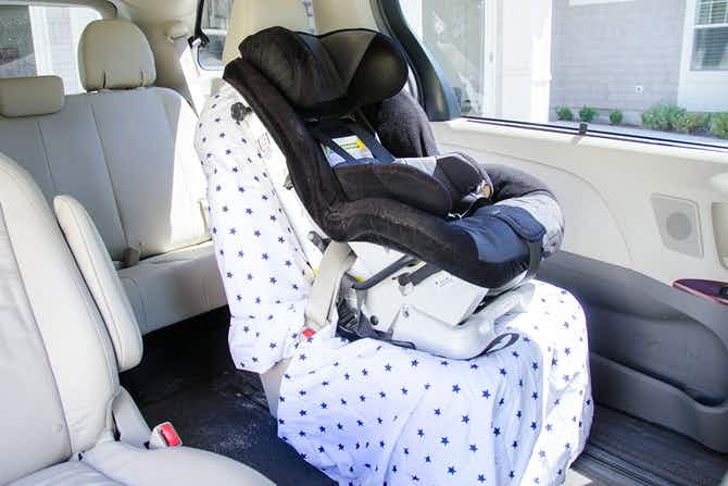 A baby car seat fastened onto a seat in a van that is covered by a fitted sheet.