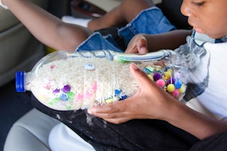A child sitting in a car, looking into a clear plastic water bottle that has been filled with rice and various trinkets to play iSpy.