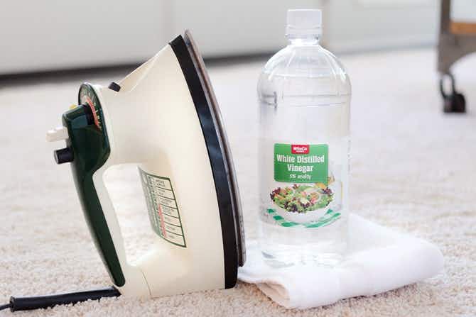 An iron next to a bottle of white vinegar and a white towel. 