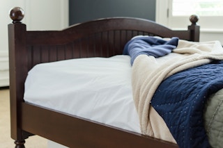 A bed with a shower curtain liner as a mattress protector with blankets on top.