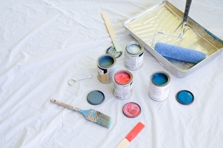 A drop cloth with cans and a tray of paint.