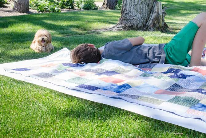 A boy laying on a blanket over a shower curtain liner next to a dog laying on the grass.
