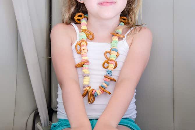 A child sitting in a car wearing a necklace made out of pretzels and cereal loops.