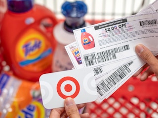 A person holding tide manufacture coupons in one hand and a Target gift card in the other, with a shopping card containing laundry detergents in the background.