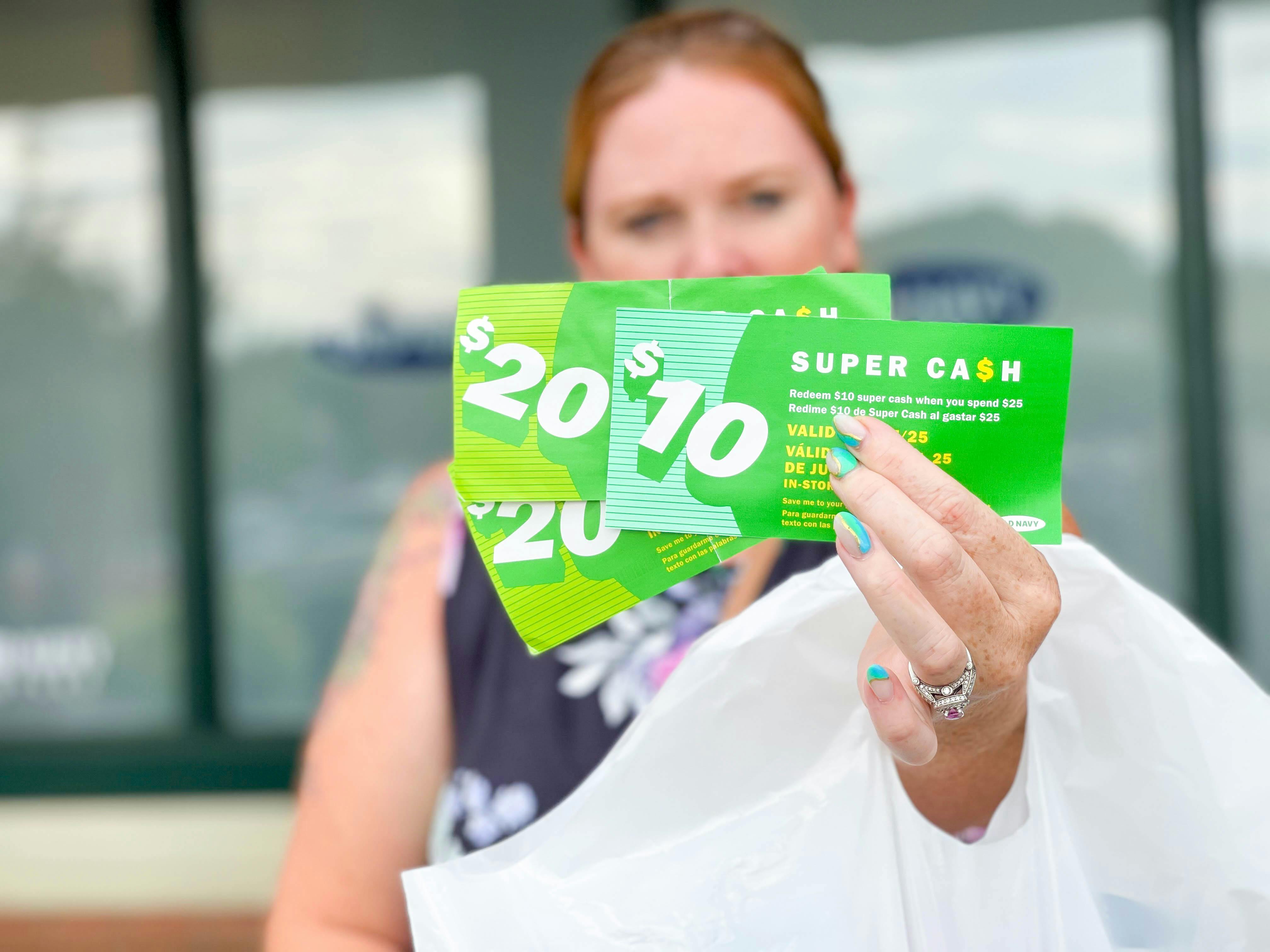 A woman holding out some Super Cash coupons outside an Old Navy store.