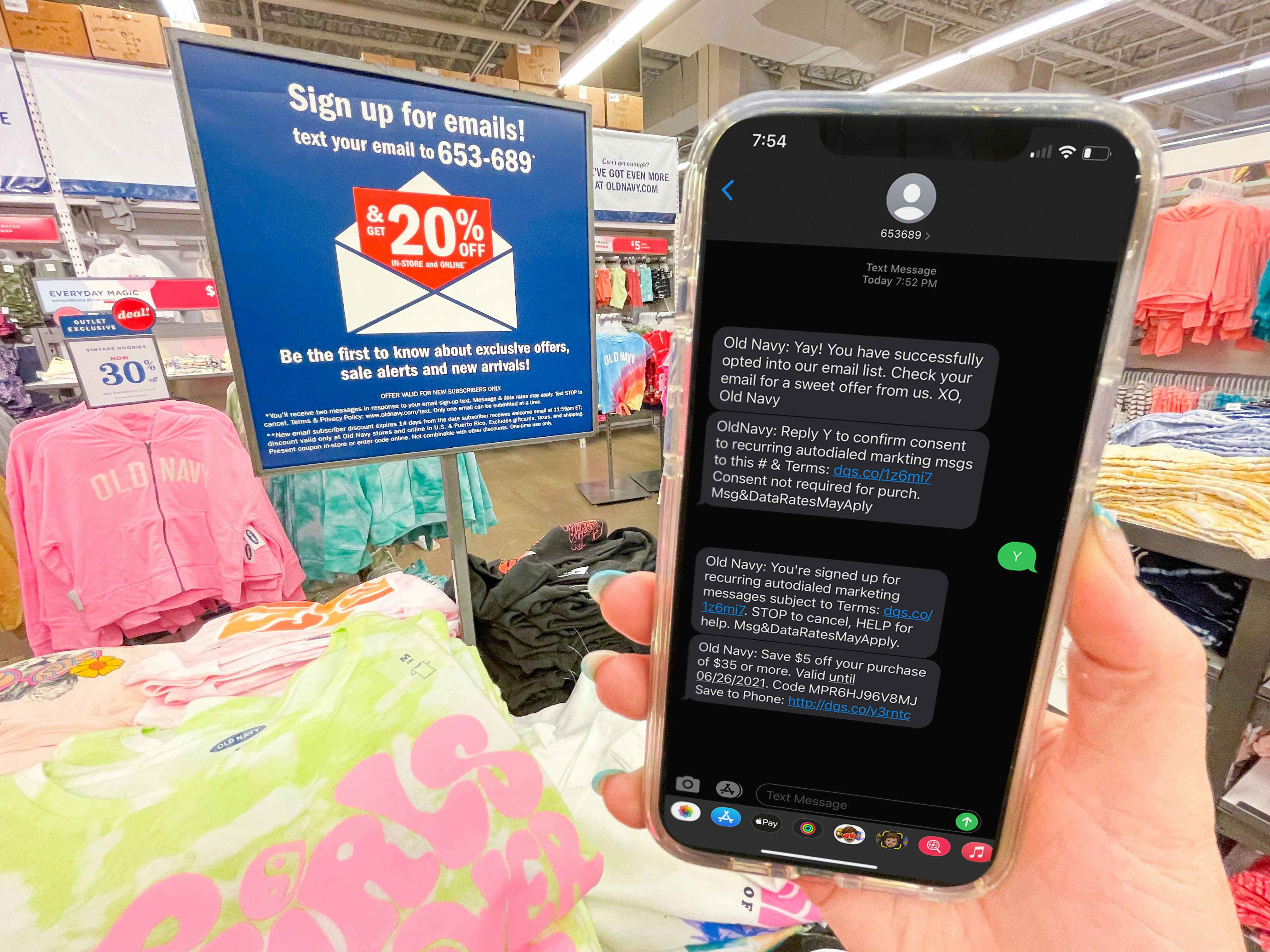 hand holding cellphone with text from old navy in front of sign for text for email