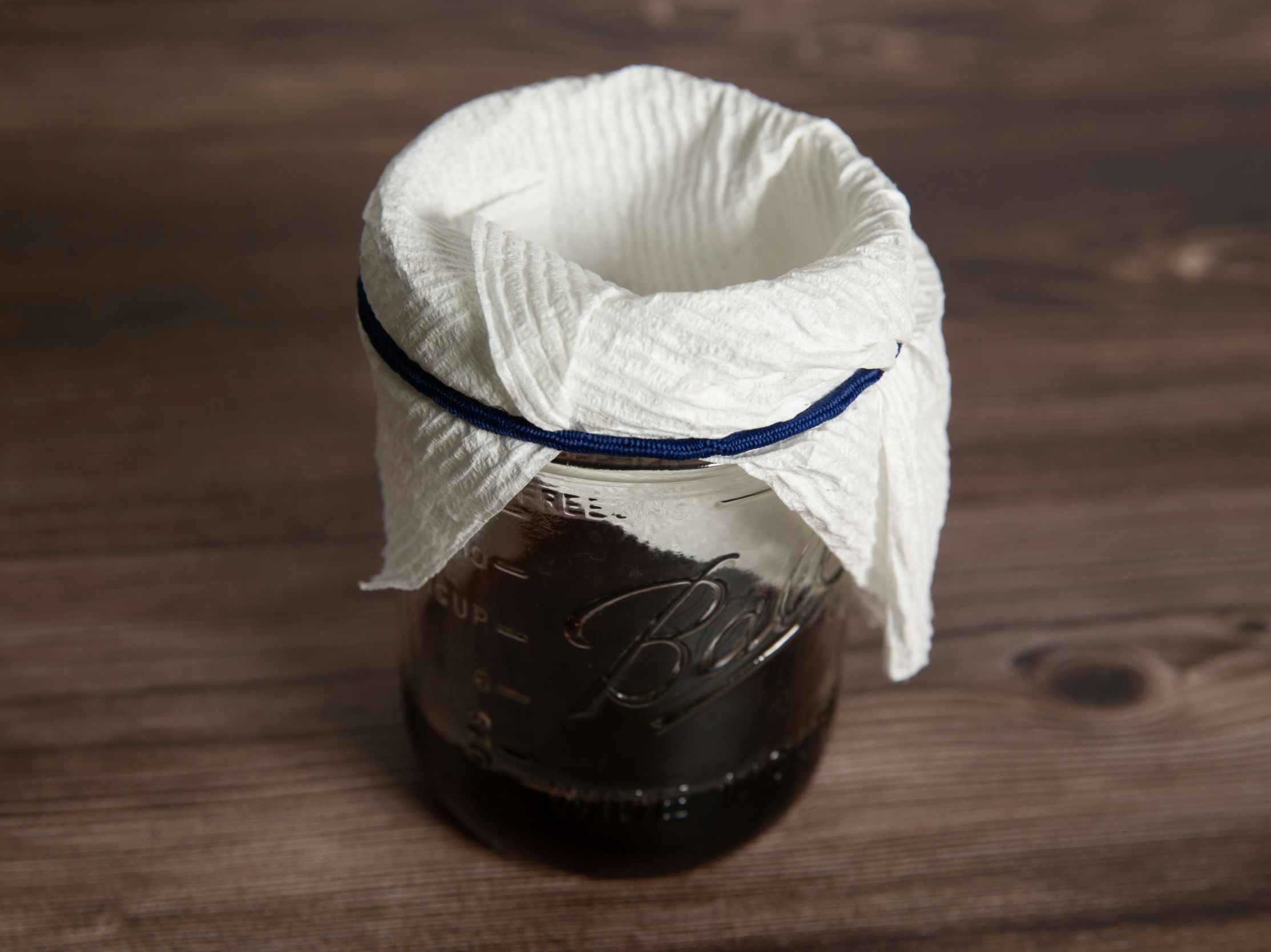 Wine in a wide mouth containter covered with a rolled paper towel