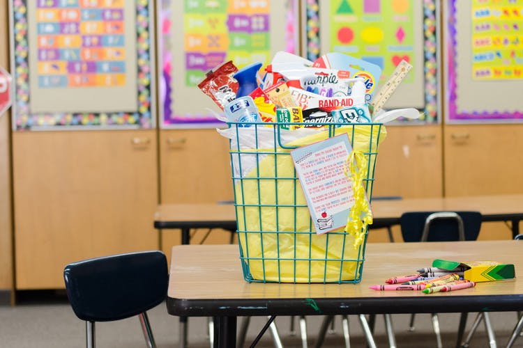 A wire basket filled with gifts for the teacher sitting on top of a child's chair in a classroom.
