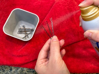 Someone spraying hairspray onto some bobby pins