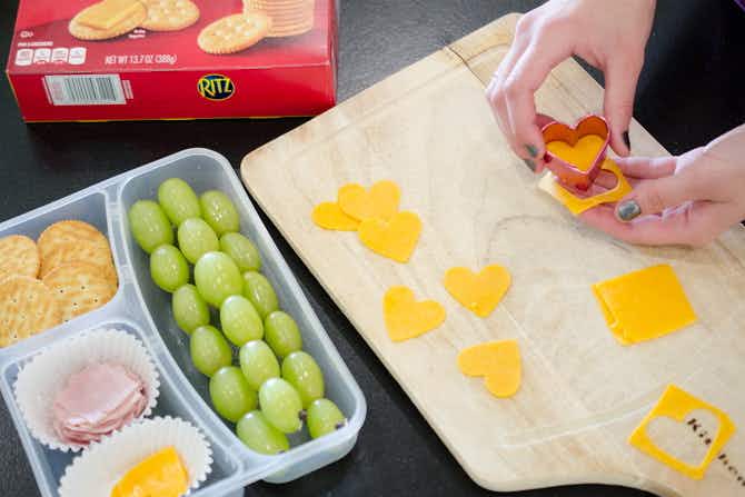 A person using a cookie cutter to cut cheese into fun shapes.
