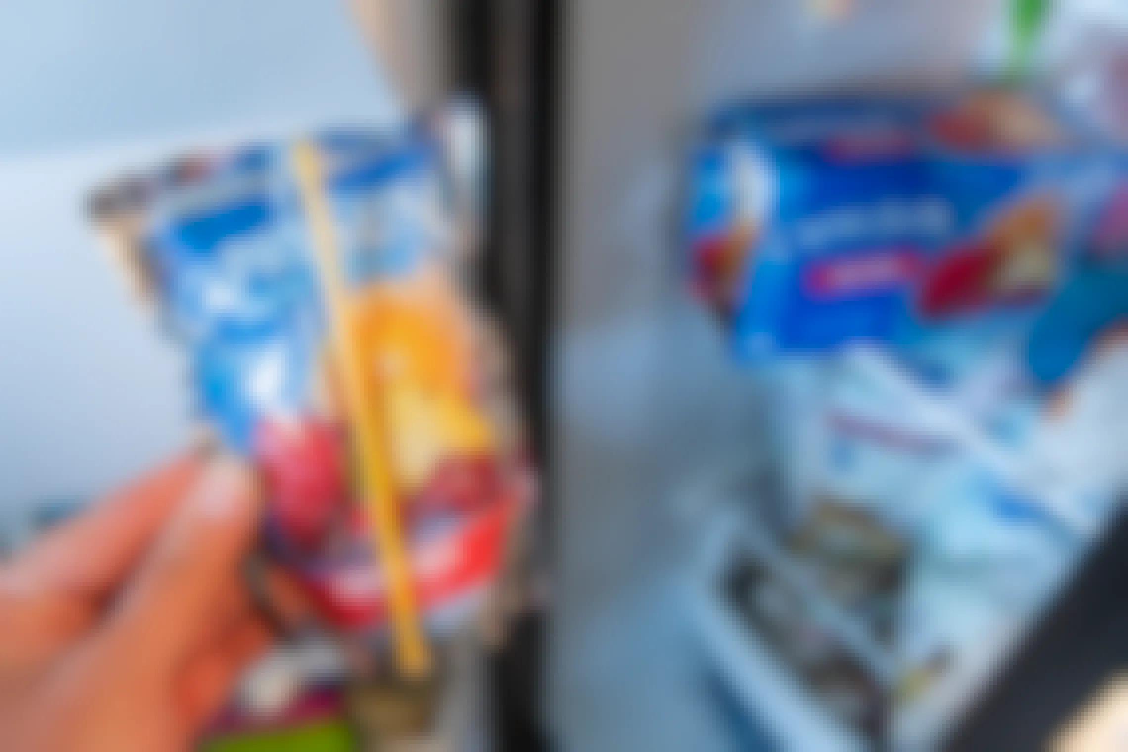 A person's hand holding a frozen CapriSun pouch next to a box of more CapriSun pouches sitting on a shelf in a freezer.