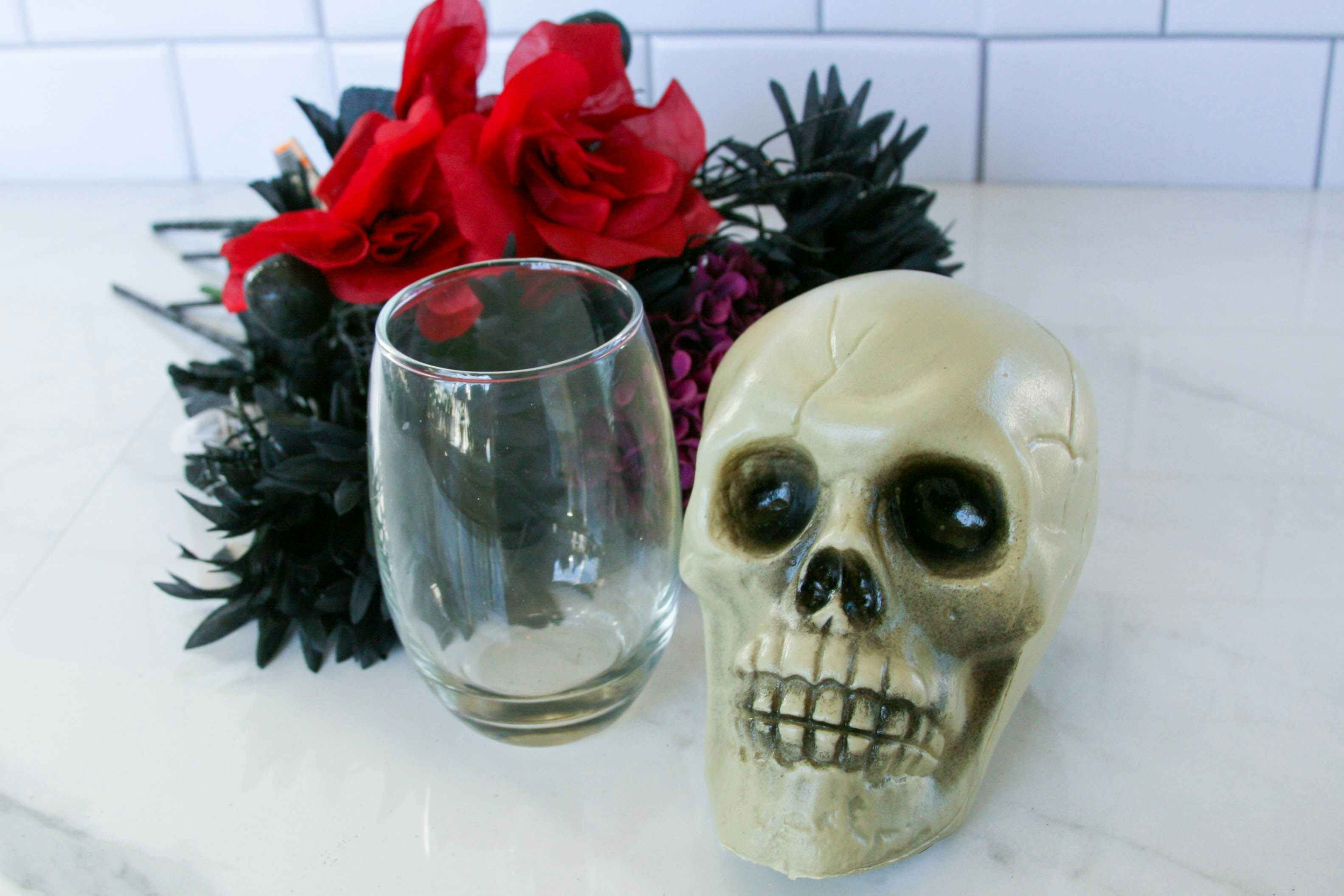 a plastic skull, drinking glass, and fake flowers ready for a diy project sitting on a counter