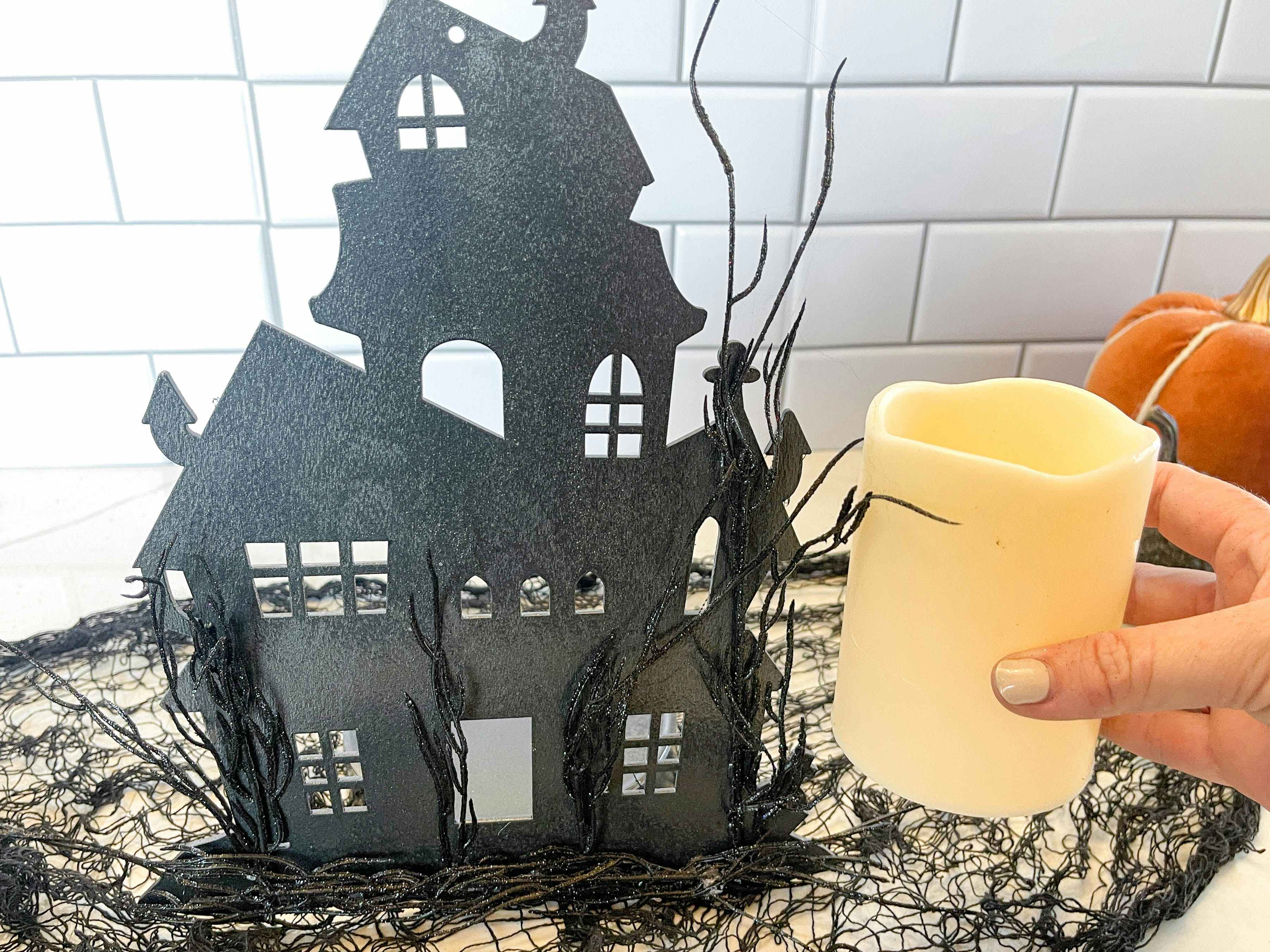 A fake candle being placed beside a diy black haunted house good cut out.