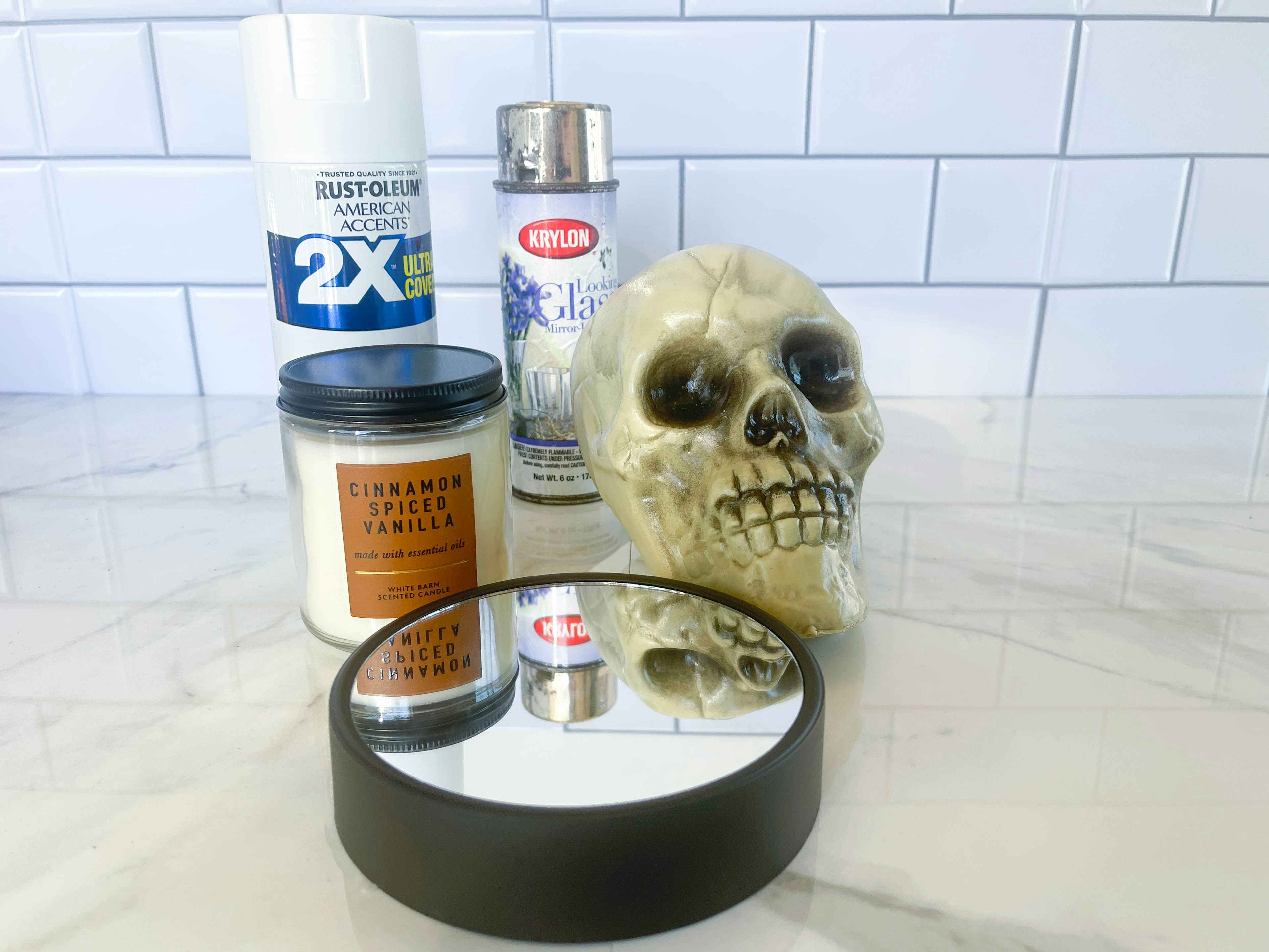 a plastic skull, mirrored candle holder, candle, and spray paint sitting on the counter ready for a diy project