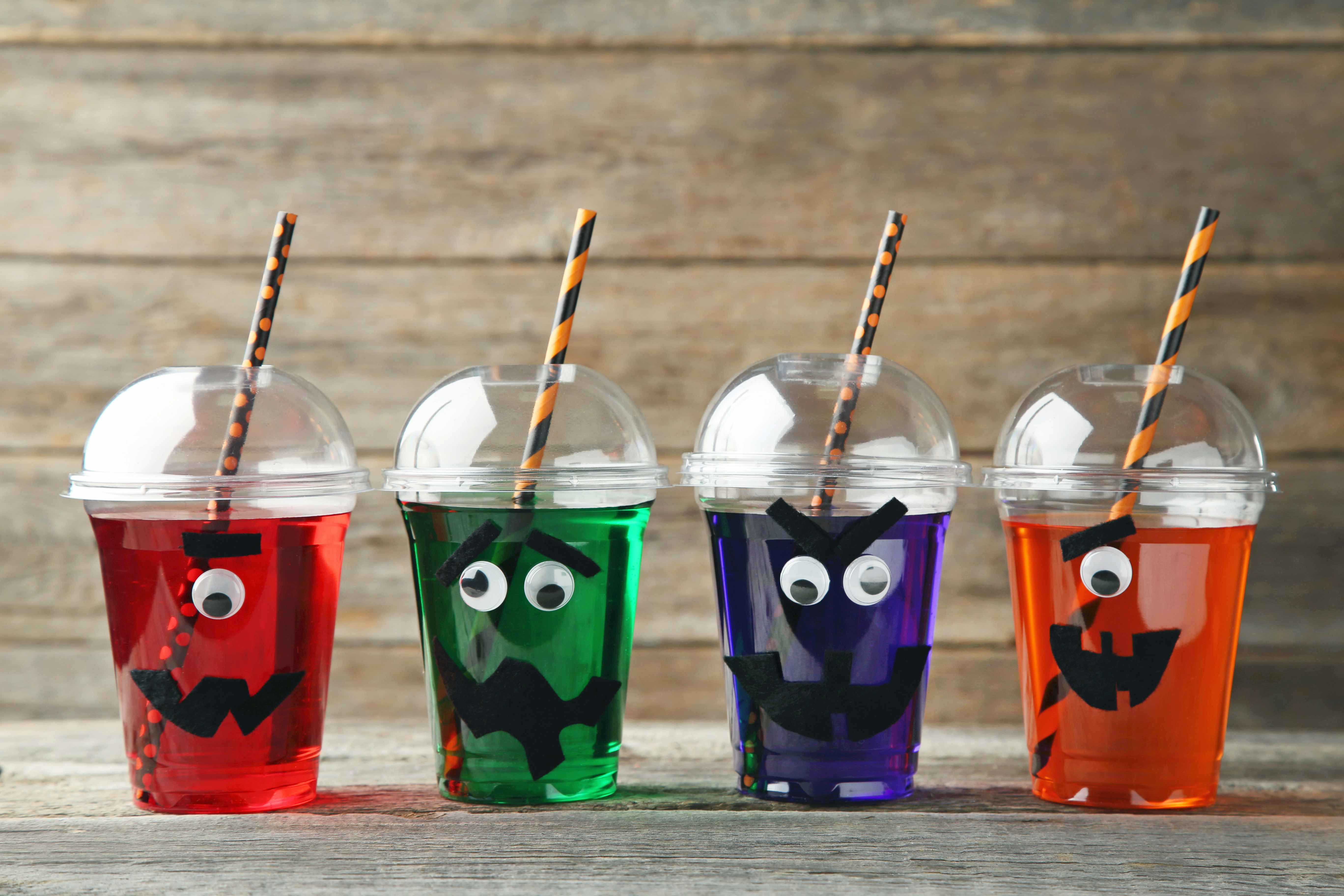 Spooky felt faces and googly eyes attached to a cup with colorful beverages and Halloween paper straws inside.