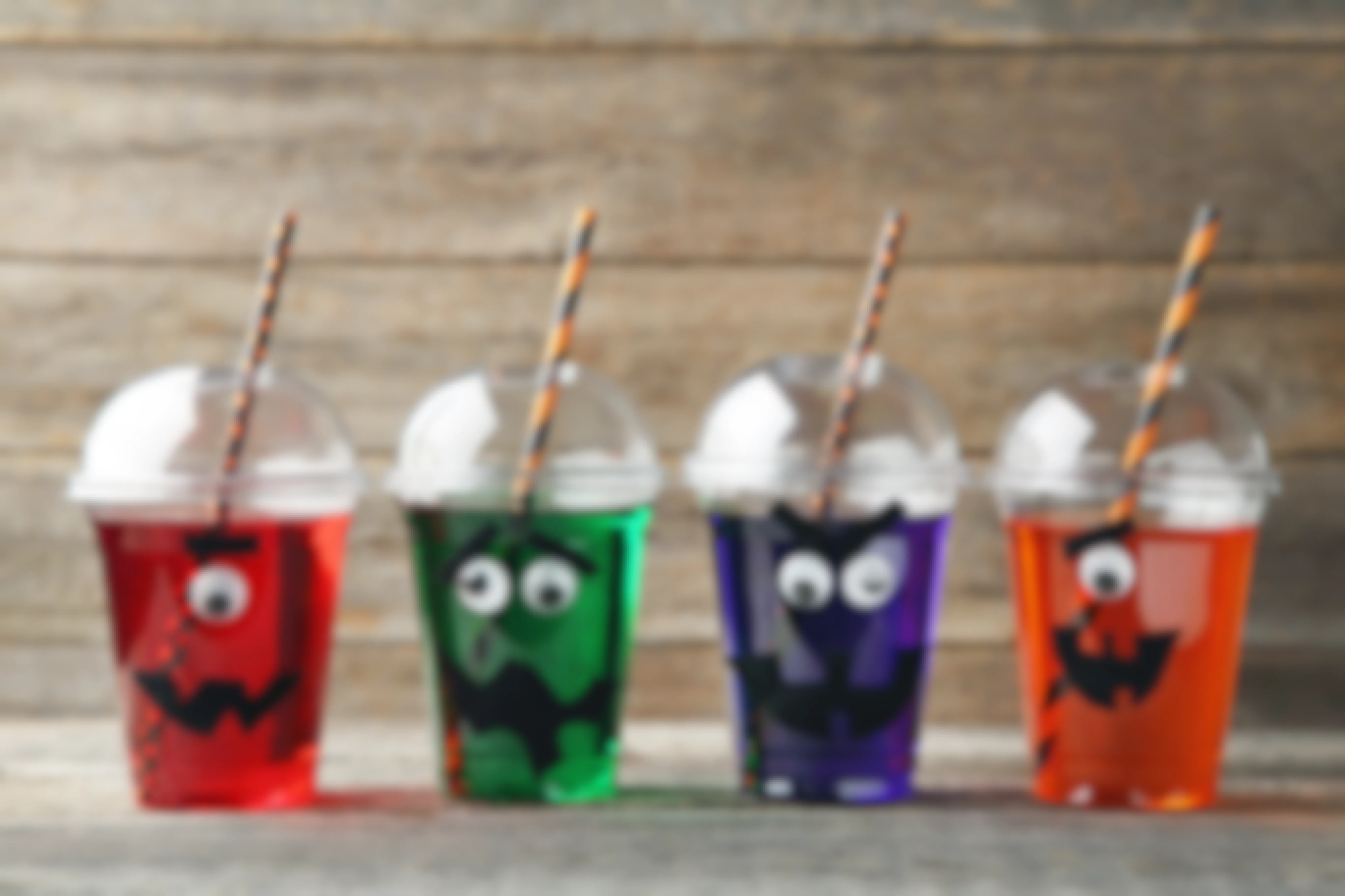Spooky felt faces and googly eyes attached to a cup with colorful beverages and Halloween paper straws inside.