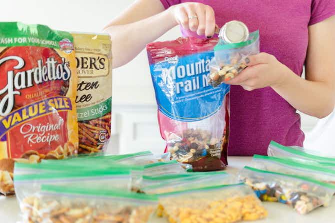 A woman using a measuring cup to separate snack mix into individual ziploc bags.