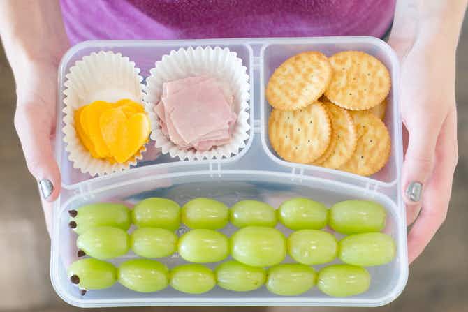 A lunch container with squares of ham and heart-shaped slices of cheese divided by muffin cups.