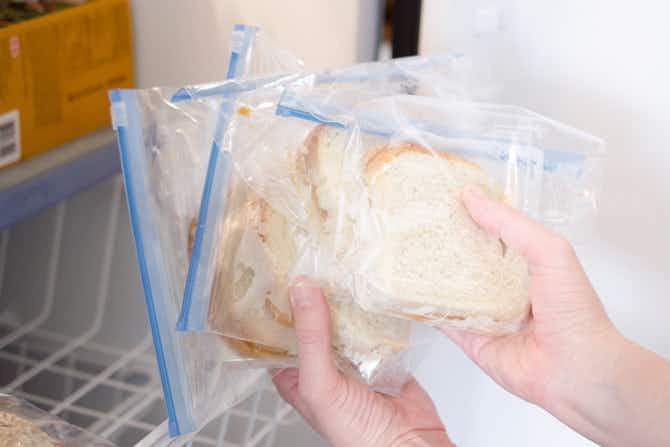 Three frozen sandwiches in ziploc bags being pulled out of a freezer.