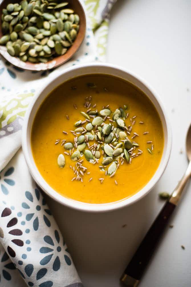 A pumpkin soup topped with pumpkin seeds in a bowl