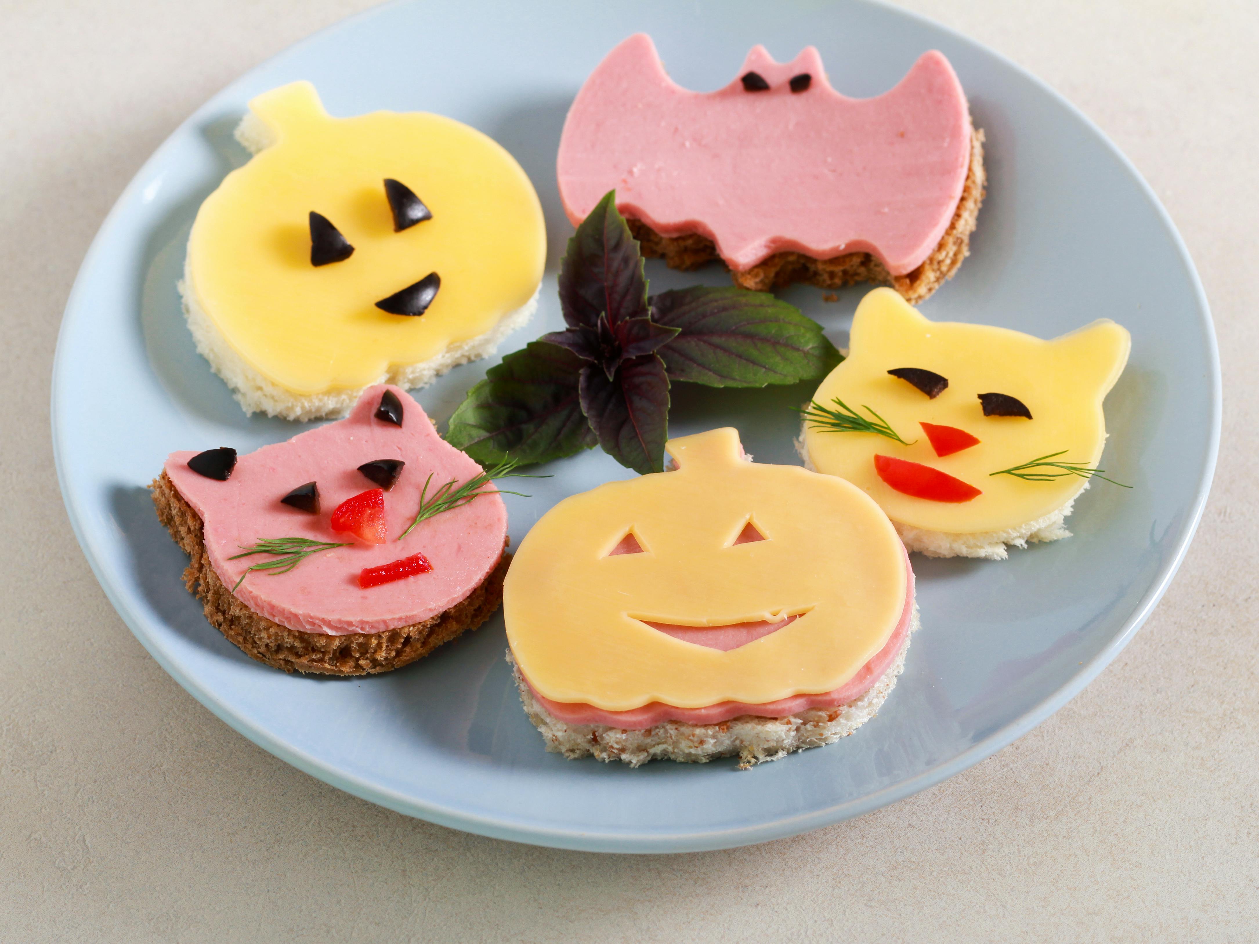 A plate of open-faced deli sandwiches with ham and cheese shaped like silly faces.