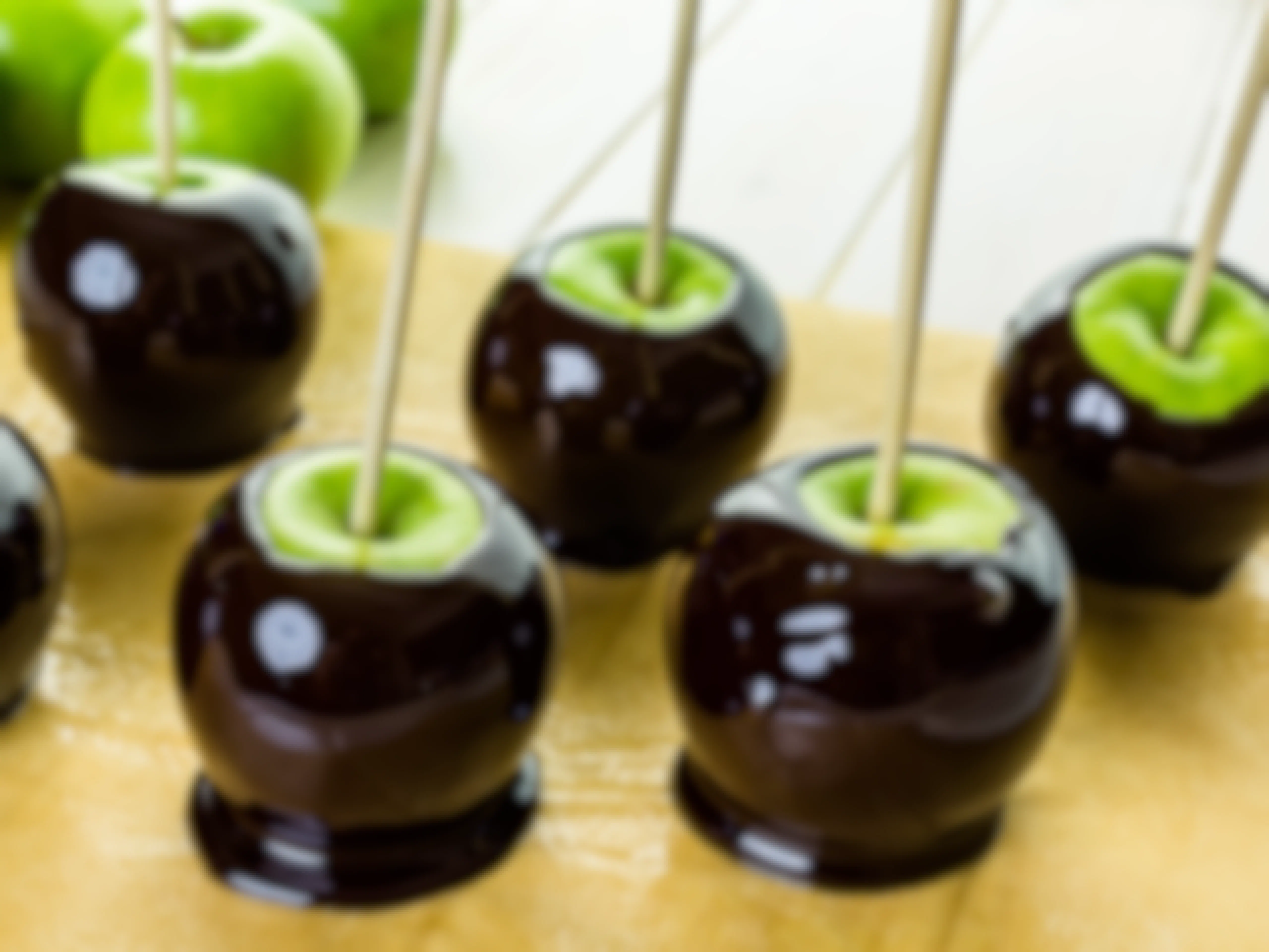 Apples dipped in black toffee candy with bamboo skewers sticking out of them, sitting on a counter.