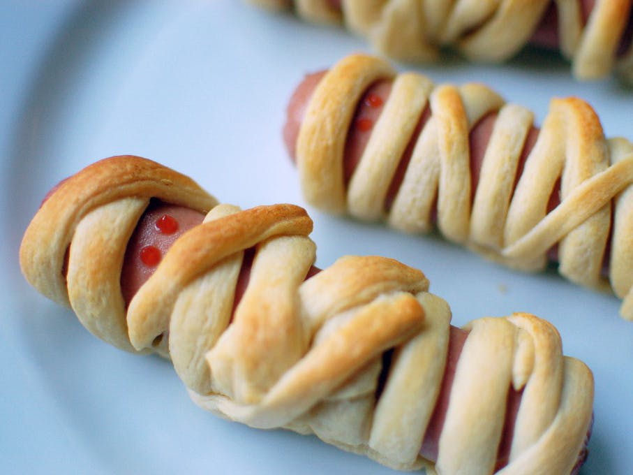 A plate of hotdogs wrapped in breading to make them look like mummies with ketchup eyes.