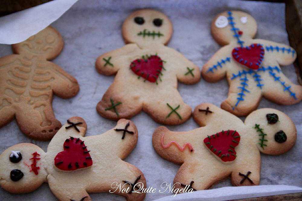 Cookies shaped and decorated to look like voodoo dolls on a cookie sheet pan lined with parchment paper.