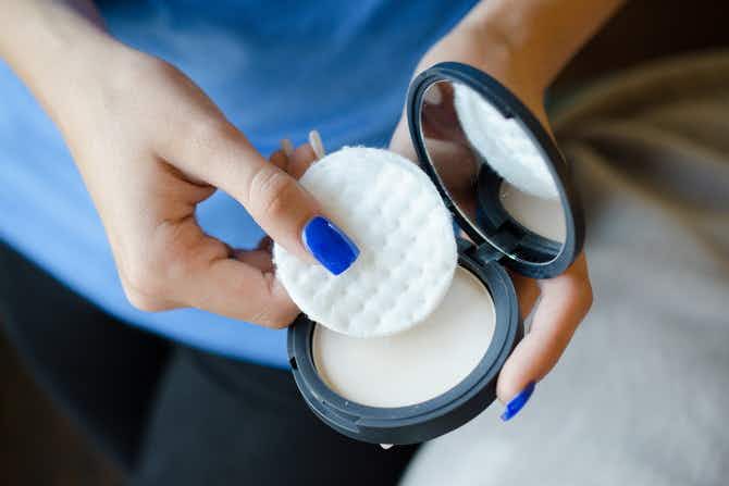 a woman placing a cotton pad in a compact makeup case
