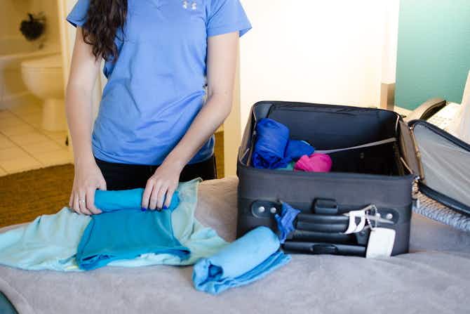 A woman rolling clothes near a suitcase