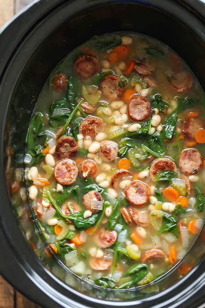 A slow cooker with sausage, spinach, celery, and carrot soup