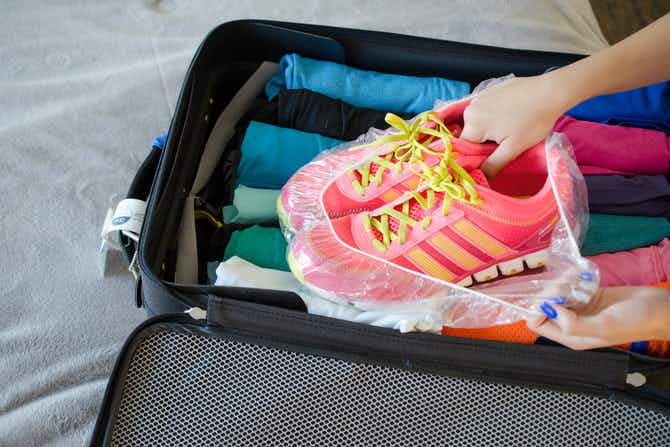 woman placing tennis shoes in a shower cap in luggage